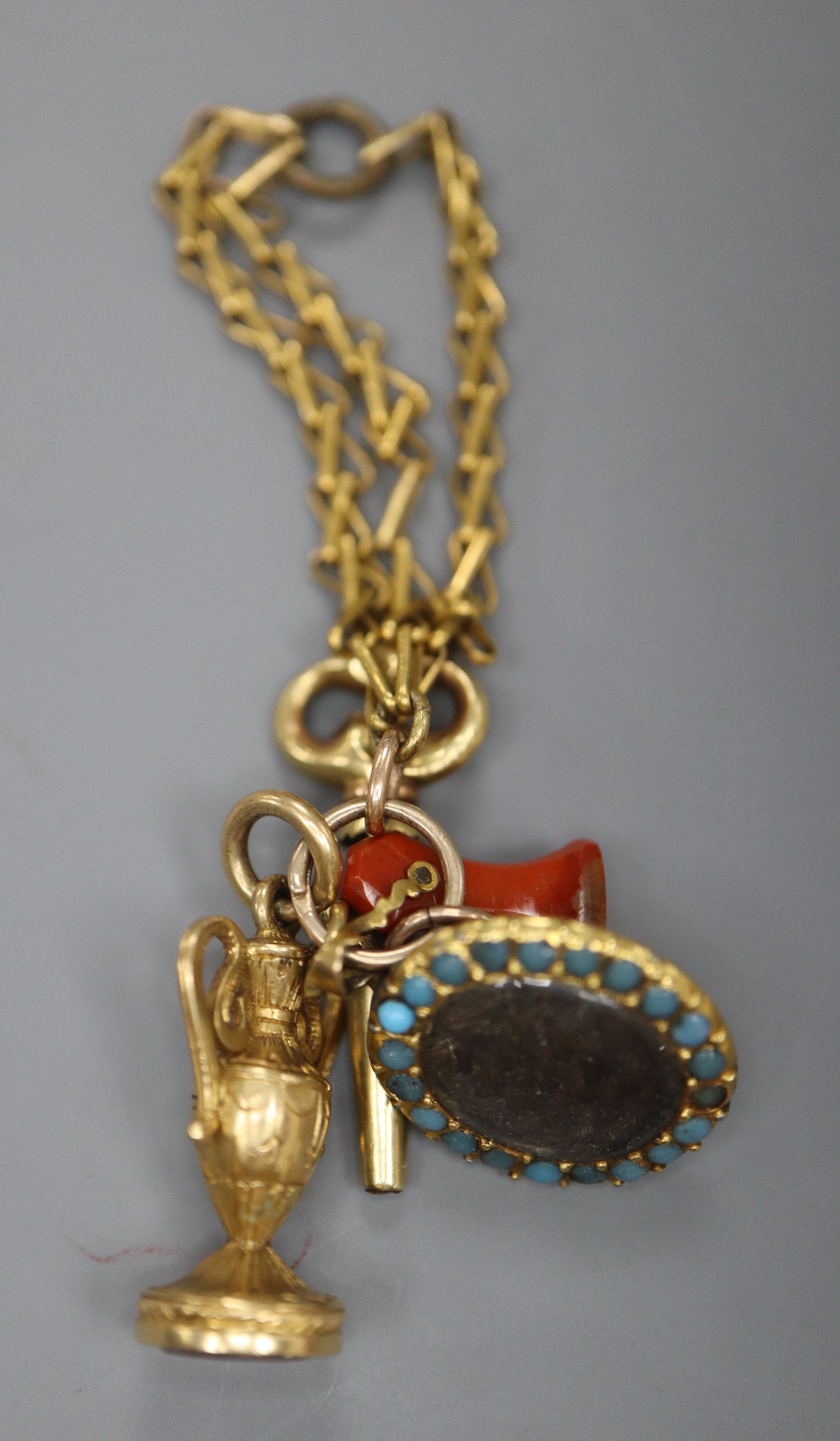 A group of four assorted charms on a yellow metal small chain, including a watch key and small carnelian seal.